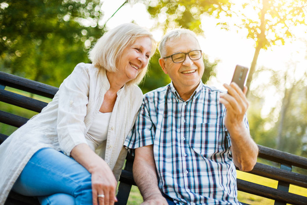 Gelukkige senior paar is het gebruik van smartphone in park. - Foto, afbeelding