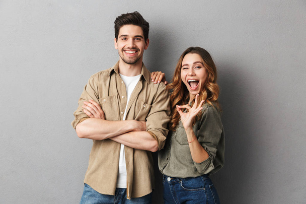 Portrait of a cheerful young couple standing together isolated over gray background, showing ok - Foto, Imagem