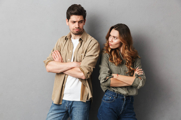 Portrait of an upset young couple having an argument isolated over gray background, looking at each other - Photo, image