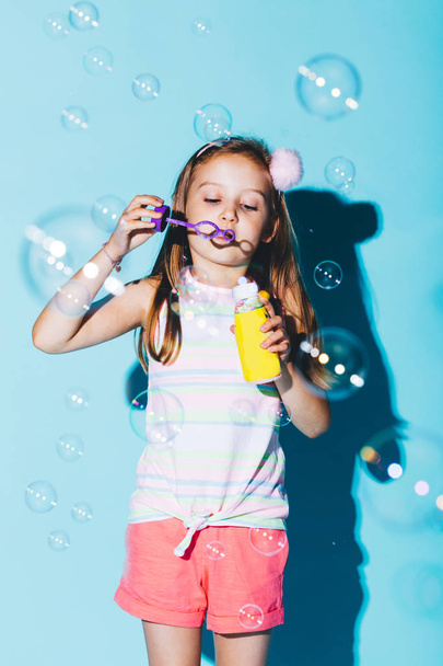 Bambina che soffia bolle di sapone su sfondo blu. Divertimento infantile
. - Foto, immagini