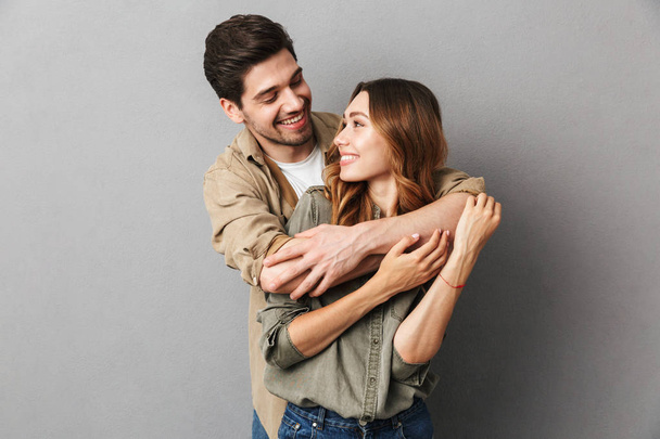 Portrait of a happy young couple hugging isolated over gray background - Foto, Bild