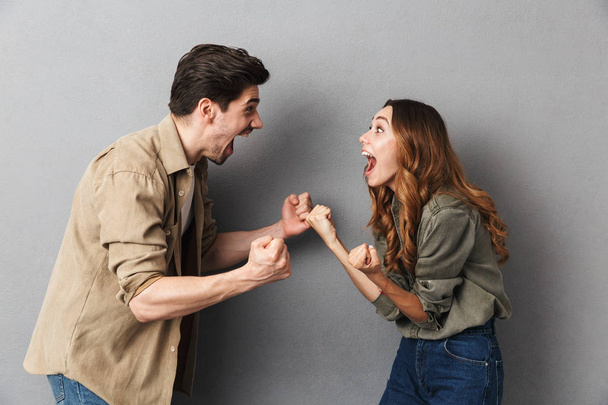 Portrait of a happy young couple screaming and looking at each other isolated over gray background - Photo, image