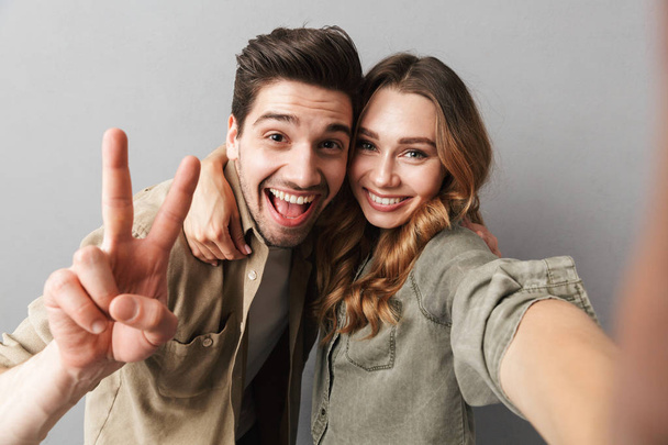 Portrait of a happy young couple hugging while taking a selfie isolated over gray background - Fotó, kép