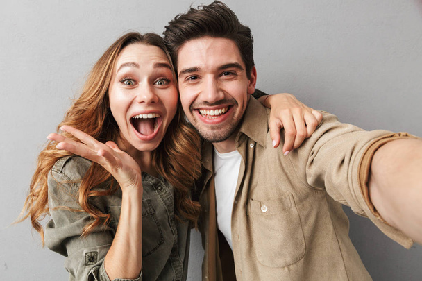 Portrait of an excited young couple hugging while taking a selfie isolated over gray background - Foto, Imagem