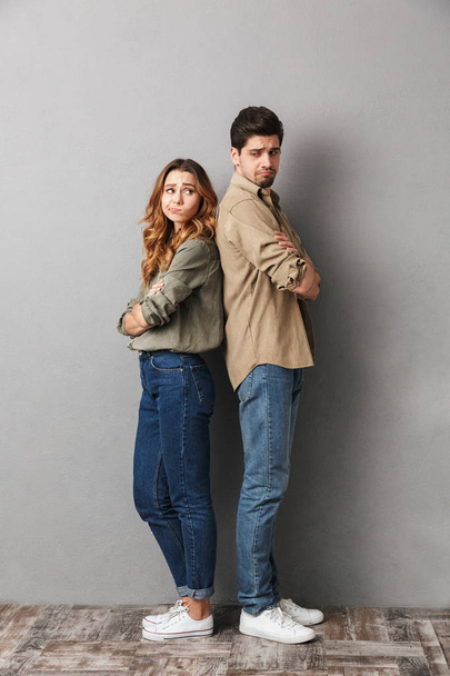 Full length portrait of a sad young couple standing back to back with arms folded isolated over gray - Foto, Imagem