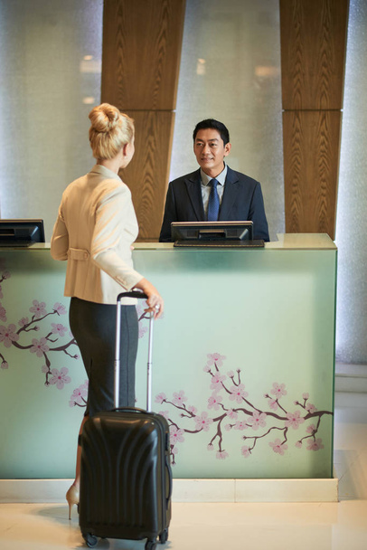 Woman with big suitcase checking in at hotel reception - Foto, Imagem