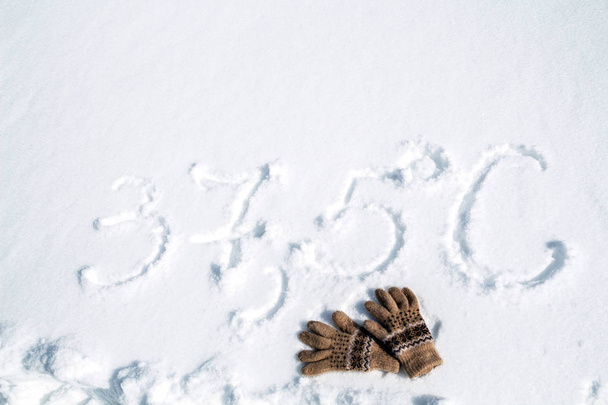 napis na śniegu temperatura 37,5 i dwie rękawice leżące na śniegu. - Zdjęcie, obraz