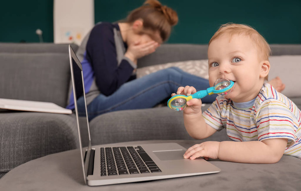 Bebê bonito com laptop com mãe cansada em casa
 - Foto, Imagem