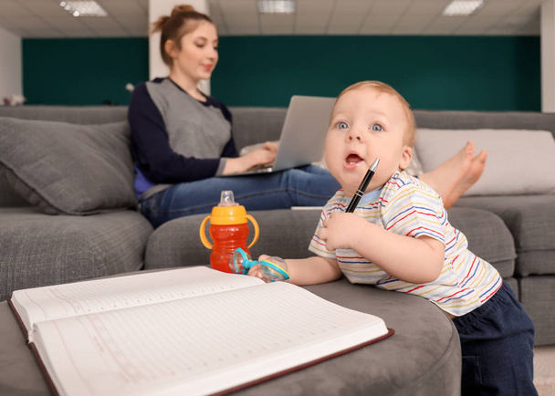 Niedliches kleines Baby spielt mit Notizbuch, während Mutter zu Hause arbeitet - Foto, Bild