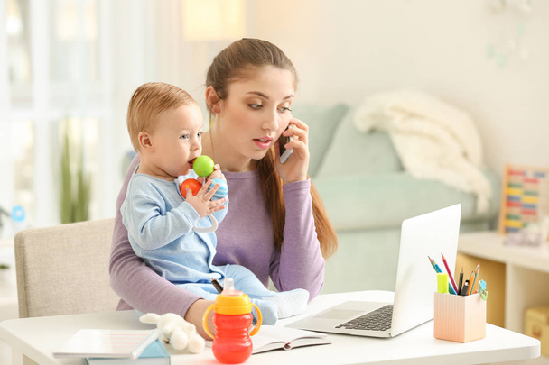 Молода мати з дитиною розмовляє по телефону під час роботи вдома
 - Фото, зображення