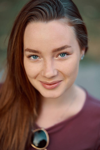 Lächeln junge Frau Nahaufnahme Porträt im Freien. rötliche junge Frau mit blauen Augen posiert vor der Kamera. - Foto, Bild
