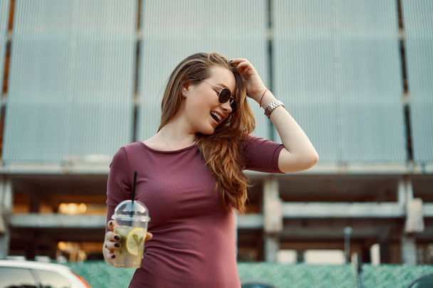 Mujer sonriente pensativa y descuidada en la calle bebiendo limonada refrescante. Concepto matutino
. - Foto, imagen