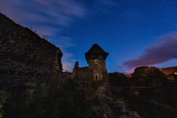 Ruins of medieval castle at night with amazing starry sky and clouds, mystical place, Nevytsky castle, Transcarpathia, Ukraine, Eastern Europe - Photo, Image