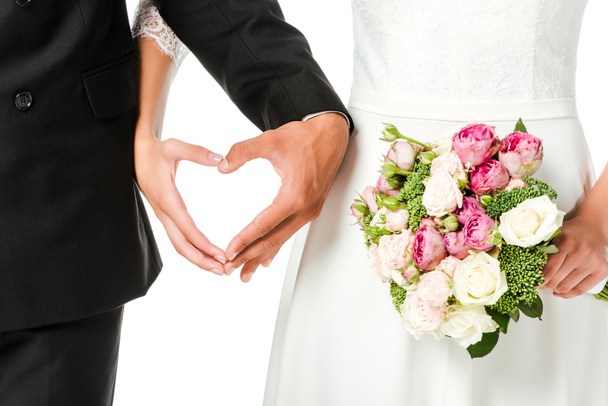 cropped shot of bride with bouquet and groom making heart sign with hands isolated on white - Φωτογραφία, εικόνα