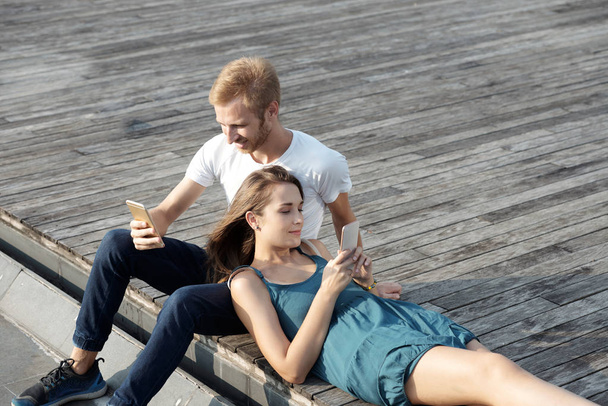Νεαρό ζευγάρι αναπαύεται σε εξωτερικούς χώρους και την ανάγνωση μηνυμάτων σε smartphone - Φωτογραφία, εικόνα