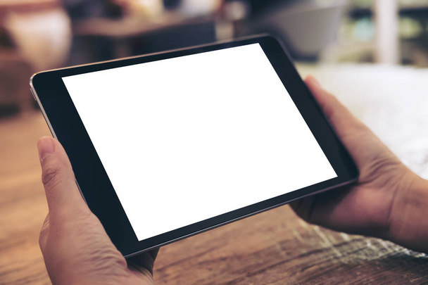 Imagen burlona de manos sosteniendo pc tableta negra con pantalla blanca en blanco sobre fondo de mesa de madera en la cafetería
 - Foto, Imagen