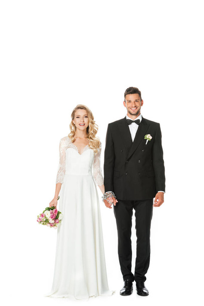 happy young bride and groom holding hands and looking at camera isolated on white - Photo, Image