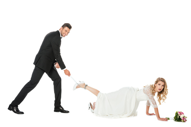 happy groom holding chain tied around brides leg and looking at camera isolated on white - Photo, Image