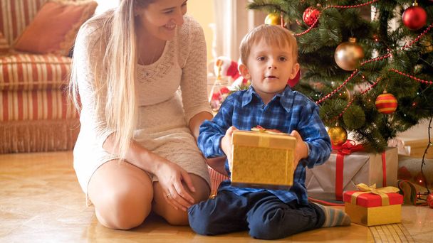 Portrait of adorable toddler boy holding christmas gift he received from mother at morning - Foto, Imagen