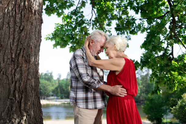 Starsza pani przytulanie opiekuńczego męża Brodaty stojący w pobliżu rzeki - Zdjęcie, obraz