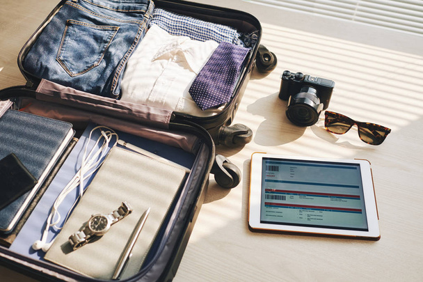 Primer plano de la maleta para un nuevo viaje y touchpad con billete electrónico sobre la mesa
 - Foto, Imagen