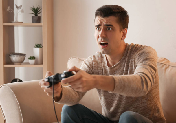 Молодий чоловік грає у відеогру вдома
 - Фото, зображення