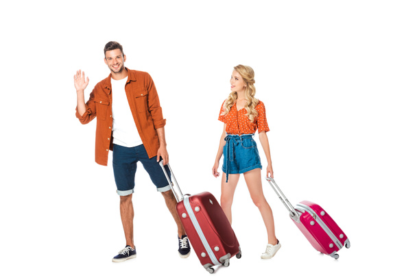happy young couple with luggage walking and waving at camera isolated on white - Фото, зображення