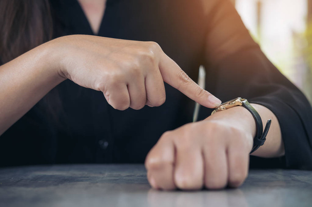 Μια γυναίκα των επιχειρήσεων κατάδειξης σε ένα μαύρο ρολόι στο χέρι στον χρόνο εργασίας κατά την αναμονή για κάποιον με αίσθηση θυμωμένος - Φωτογραφία, εικόνα