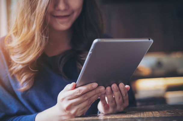 Eine schöne Asiatin mit Smiley-Gesicht hält und benutzt Tablet-PC in modernem Café - Foto, Bild