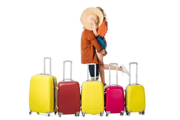 obscured view of newlywed couple kissing behind straw hat with arranged suitcases around isolated on white - Photo, Image