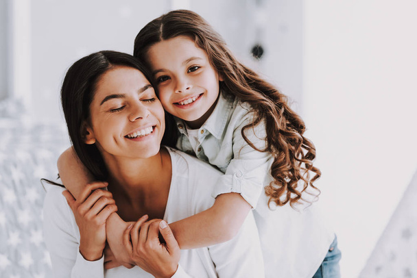 Young Mother and Smiling Little Daughter Hugging. Happy Adorable Little Girl Hugging Adult Woman near Winwow. Young Woman and Cute Daughter Together. Family and Motherhood Concept - Фото, изображение