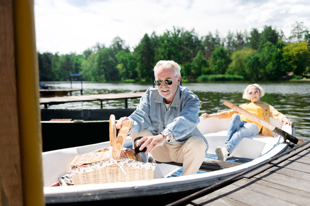 Bearded elderly man wearing jeans jacket taking bottle of wine - Fotografie, Obrázek