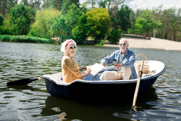 Beaming fashionable pensioners having snack during their boat ride - Foto, imagen