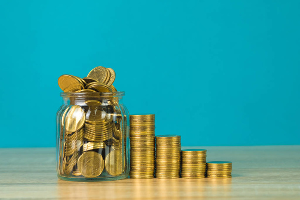 Coins stacks and gold coin money in the glass jar on table with green background, for saving for the future banking finance concept idea. - Foto, imagen