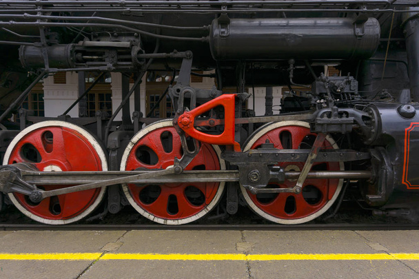 fragment de locomotive à vapeur vintage fonctionnant debout à la gare, gros plan, roues motrices visibles avec un système de pistons, bielles et leviers
 - Photo, image