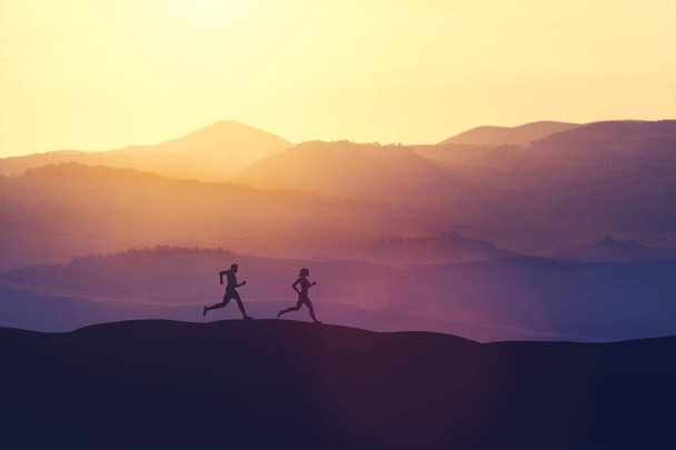 Mann und Frau laufen bei Sonnenuntergang auf einem Hügel. Sportlicher Lebensstil.  - Foto, Bild
