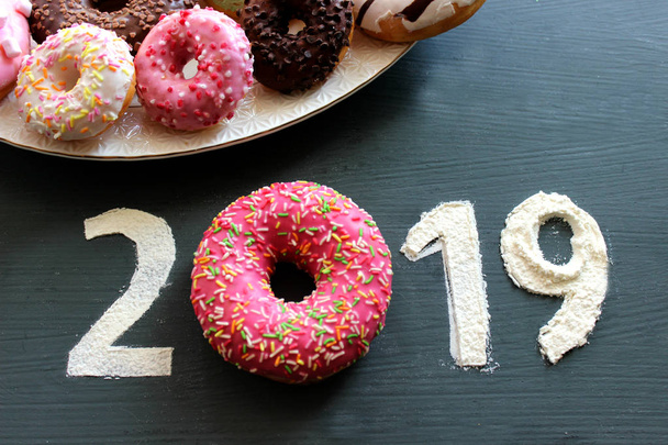 Figures 2019 on a black background filled with flour, pink donut instead of the number 0, the concept of the new year, sweet life. Free space for text - Photo, image