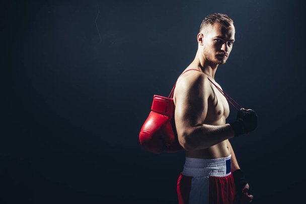 Fighter standing with gloves hanging over back. Professional sportsman. Boxing. - 写真・画像