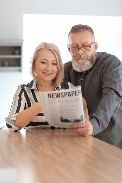Mature couple reading newspaper at home - Фото, изображение