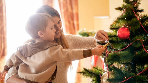 Portrait of happy smiling mother with her child decroating Christmas tree at morning - Foto, Bild