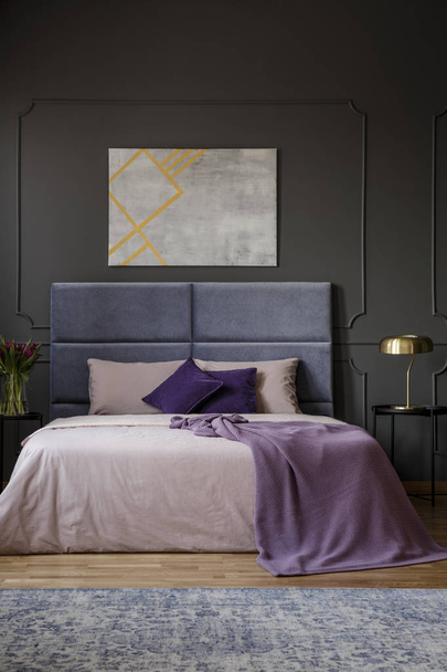 Real photo of elegant apartment interior for two people with big, purple bed and modern painting on the wall - Fotoğraf, Görsel