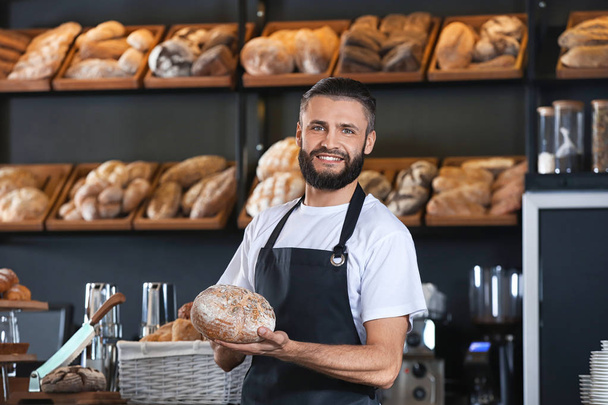 Мужчина пекарь держит свежий хлеб в магазине
 - Фото, изображение