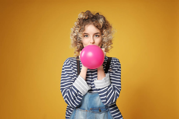 Cute young woman inflating balloon on color background - Foto, Imagem