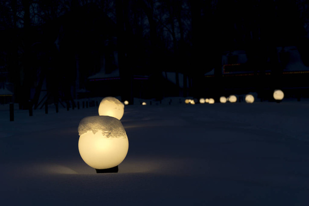 fileiras de lanternas de jardim enfadonhas e brilhantes no crepúsculo ao longo do beco de inverno coberto de neve
 - Foto, Imagem