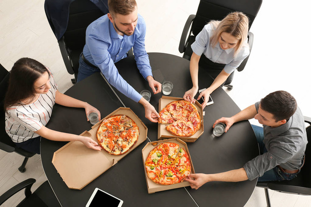 Young people eating pizza at table in office - Фото, зображення
