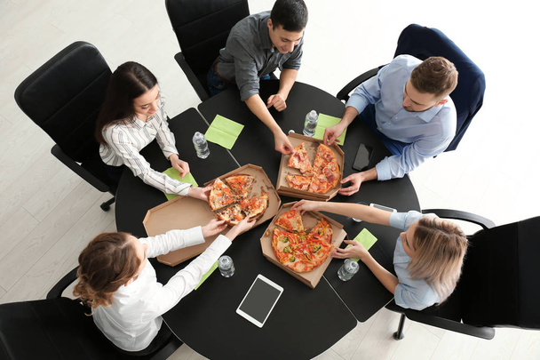 Młodzi ludzie jedzenie pizzy przy stole w biurze, widok z góry - Zdjęcie, obraz
