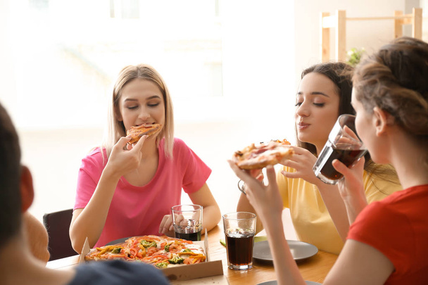 Jovens comendo pizza à mesa dentro de casa
 - Foto, Imagem