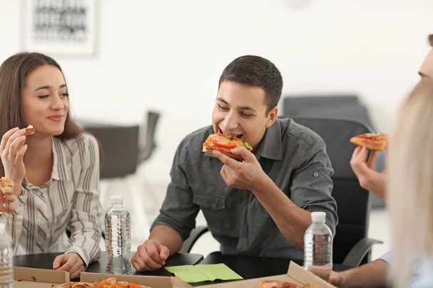 Jovens comendo pizza à mesa no escritório
 - Foto, Imagem
