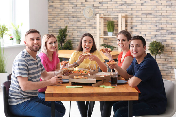 Jonge mensen eten pizza op tafel binnenshuis - Foto, afbeelding