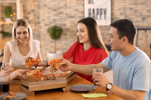 Młodzi ludzie jedzenie pizzy przy stole - Zdjęcie, obraz